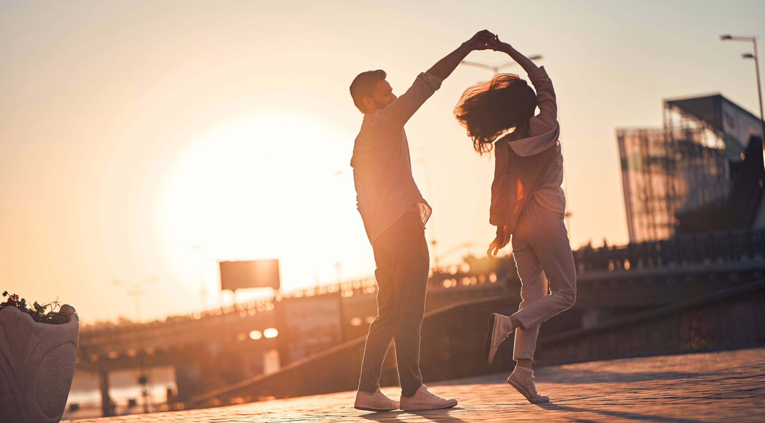 A man and woman dancing outdoors with the sunset in the background.